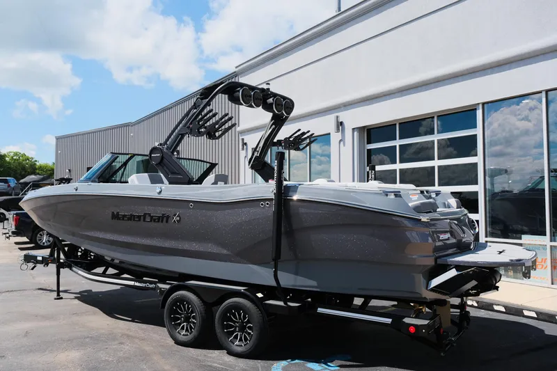 Slide: The Image of 2025 MasterCraft X26 boat on trailer, parked outside a building under a blue sky. - 44