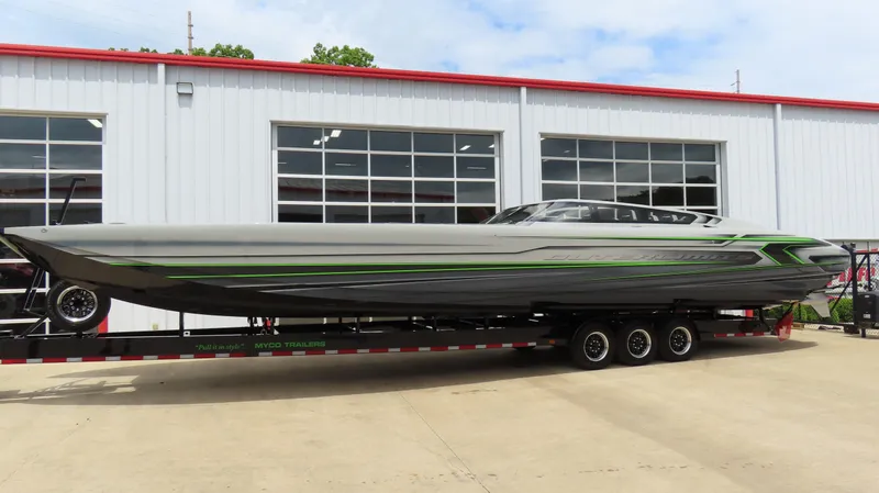 Slide: The Image of 2025 Outerlimits 46 SC powerboat on trailer, sleek design with green accents, parked outside a garage. - 1
