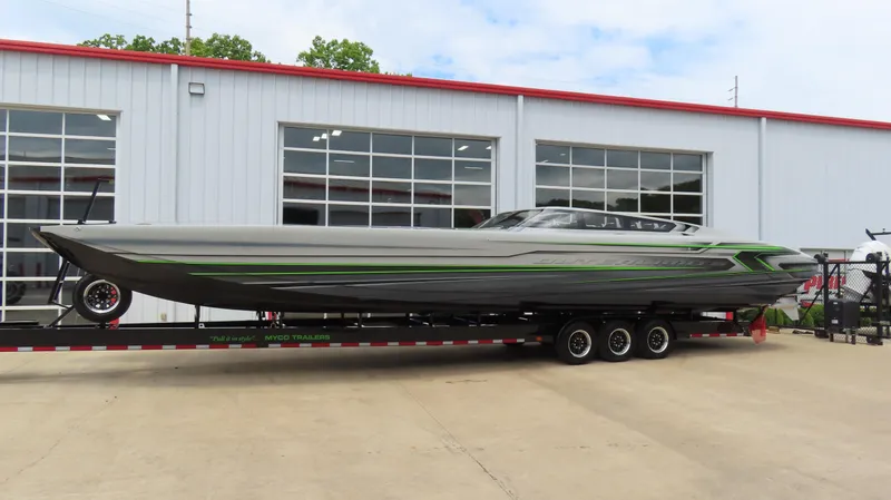 Slide: The Image of 2025 Outerlimits 46 SC powerboat on trailer, sleek design with green accents, parked outside a building. - 2
