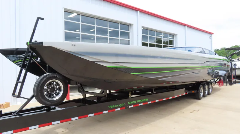 Slide: The Image of 2025 Outerlimits 46 SC powerboat on trailer, sleek design with green accents, parked outside a building. - 4