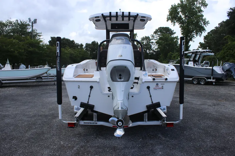 Slide: The Image of 2025 Sea Pro 245 FLX boat, rear view, parked on gravel, surrounded by trees and other boats. - 7