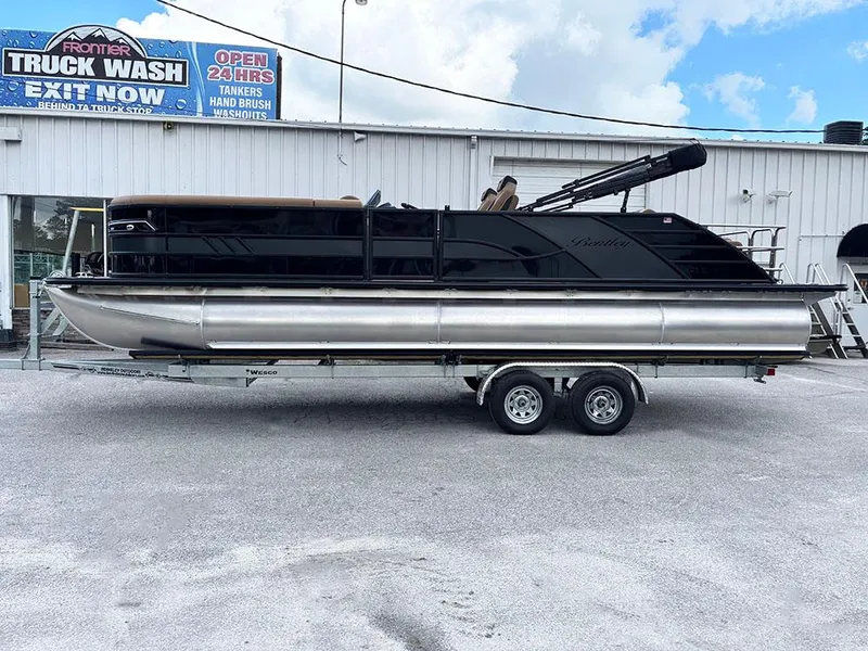 Slide: The Image of 2025 Bentley Pontoons Elite 253 Swingback Dual Captain Full Tritoon on trailer, parked outdoors. - 1