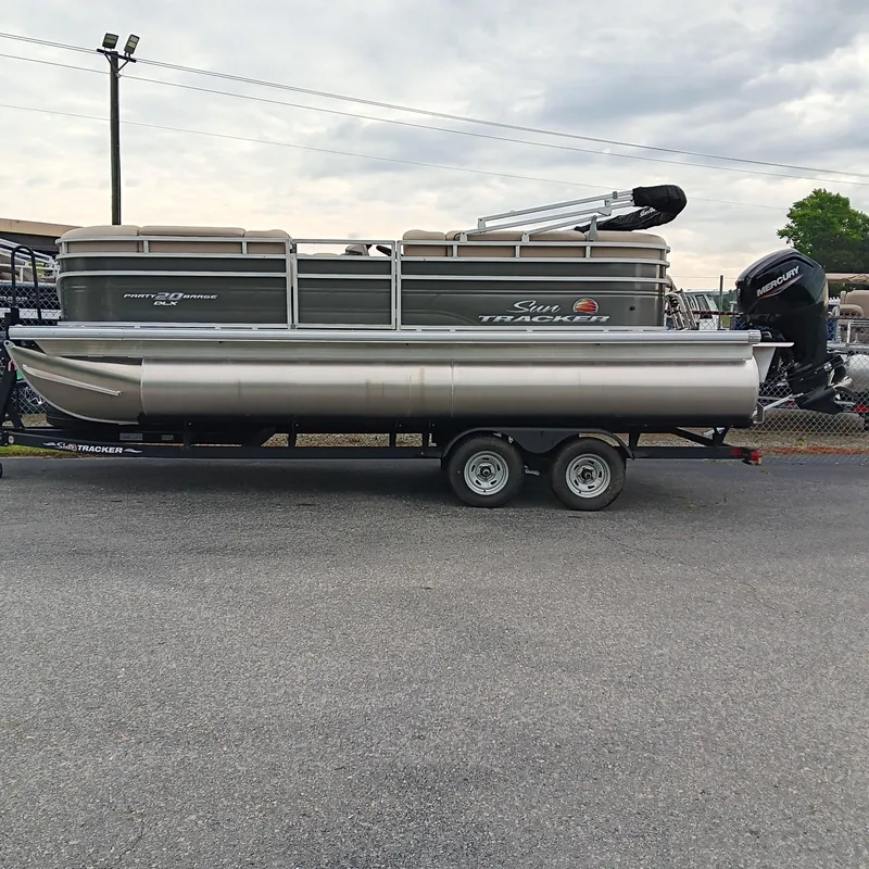 The Image of 2025 Sun Tracker Party Barge 20 DLX pontoon boat on trailer, parked outdoors. - 0