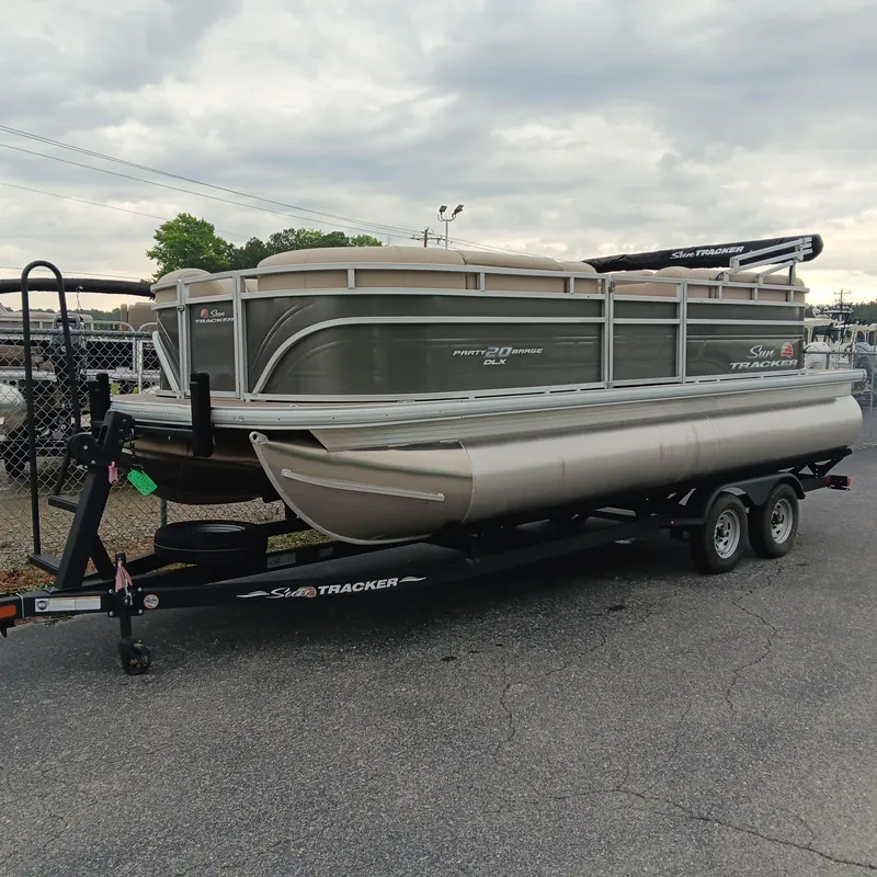 Slide: The Image of 2025 Sun Tracker Party Barge 20 DLX pontoon boat on trailer, parked outdoors. - 2