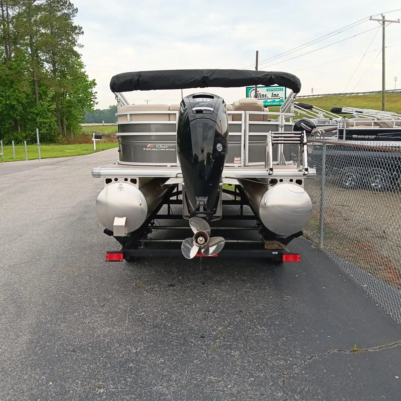 Slide: The Image of 2025 Sun Tracker Party Barge 20 DLX pontoon boat, rear view with motor, parked on pavement. - 3