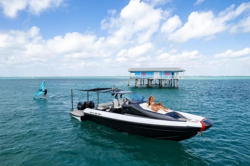 Slide: The Image of 2025 Anvera 42 Speedster boat on turquoise water near a stilt house, with windsurfer nearby. - 13