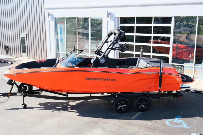 Slide: The Image of 2025 MasterCraft NXT24 boat in vibrant orange, parked on a trailer outside a showroom. - 3