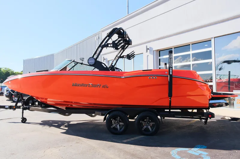 Slide: The Image of 2025 MasterCraft NXT24 boat in vibrant orange on a trailer, parked outside a building. - 4