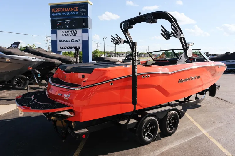 Slide: The Image of 2025 MasterCraft NXT24 boat in vibrant orange, parked at a marine dealership. - 7