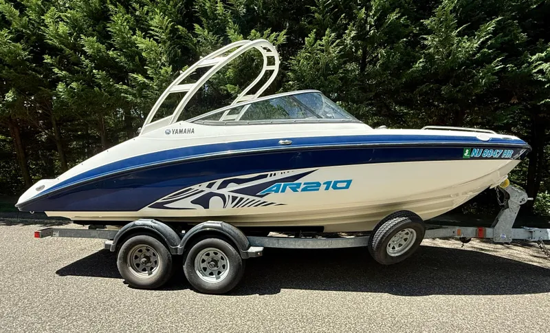 The Image of 2022 Yamaha AR210 boat on trailer, parked outdoors, surrounded by trees. - 1