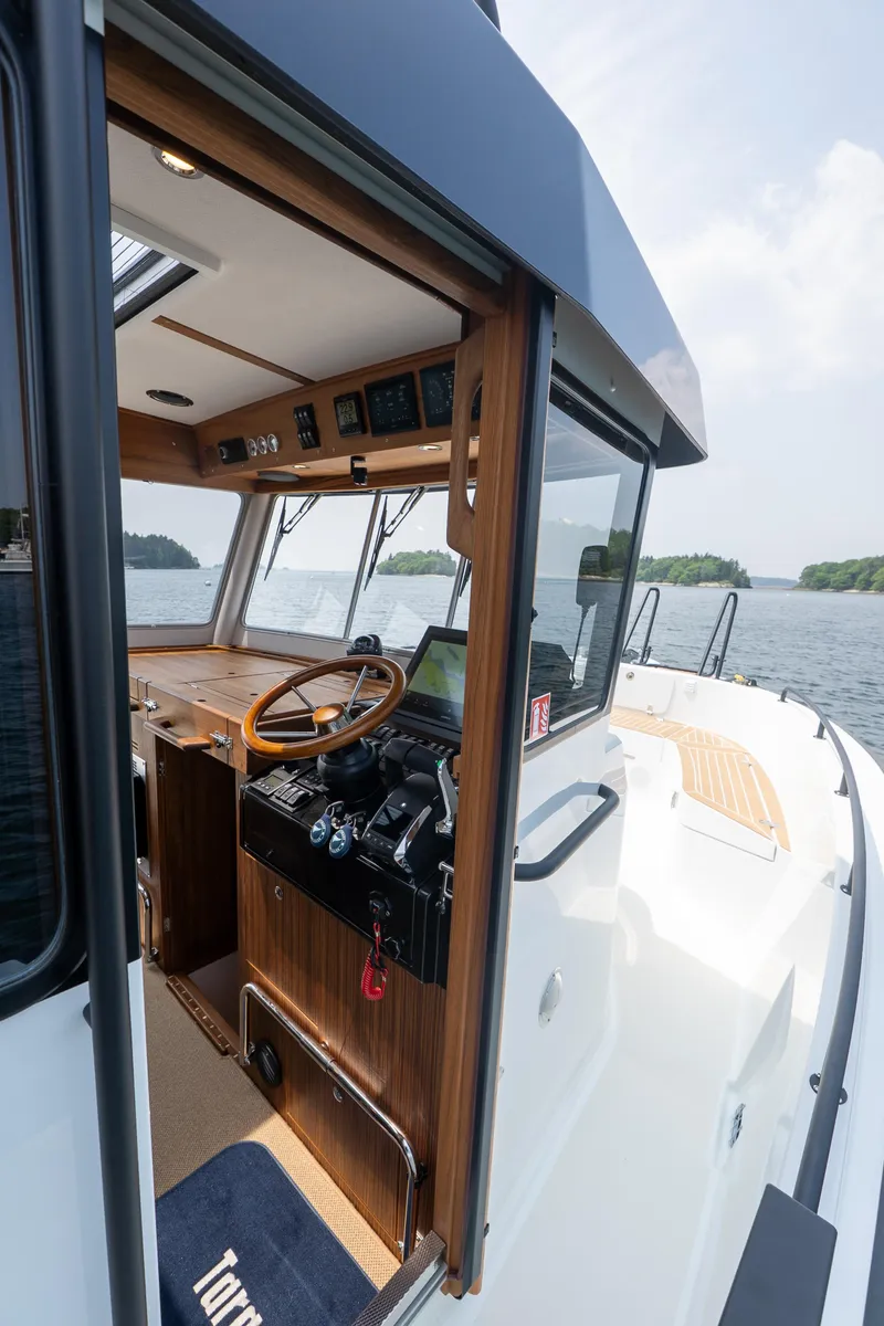 Slide: The Image of 2025 Targa 32 GT boat cockpit with wooden interior and steering wheel, on a calm lake. - 19