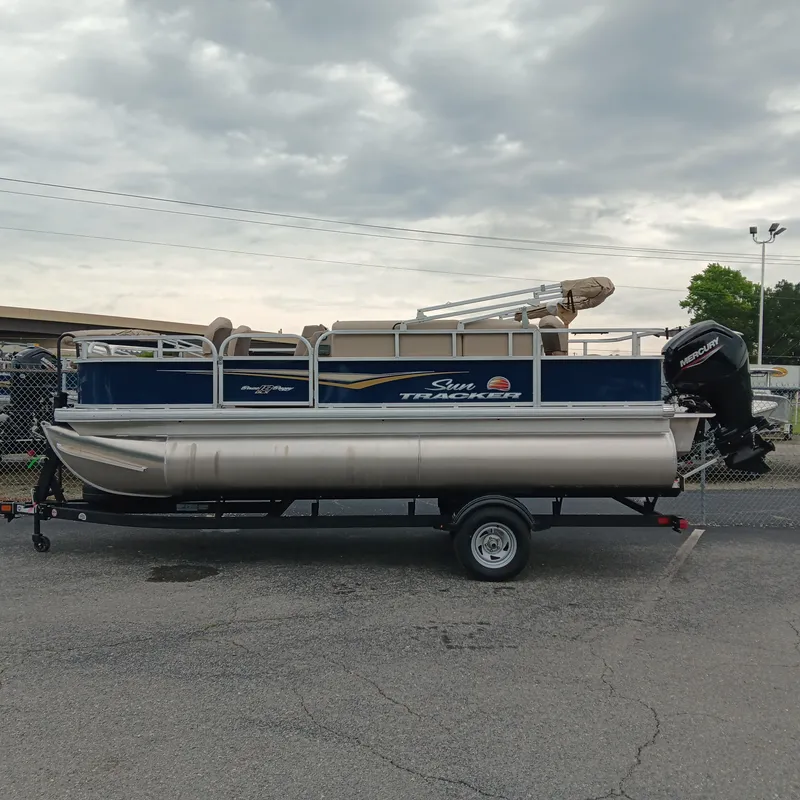 The Image of 2025 Sun Tracker Bass Buggy 18 DLX pontoon boat on trailer, parked outdoors. - 1