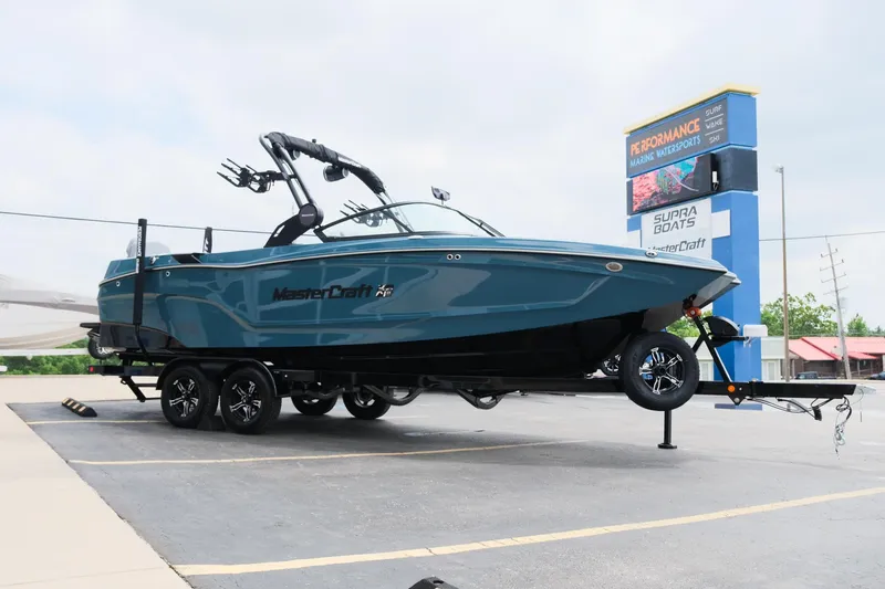 Slide: The Image of 2025 MasterCraft XT24 boat on trailer in parking lot, near dealership sign. - 12
