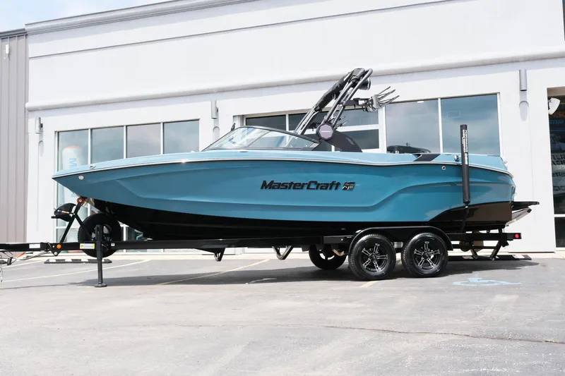 Slide: The Image of 2025 MasterCraft XT24 boat on trailer, parked outside a building. - 2