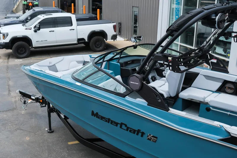 Slide: The Image of 2025 MasterCraft XT24 boat in blue, parked near white trucks. - 5