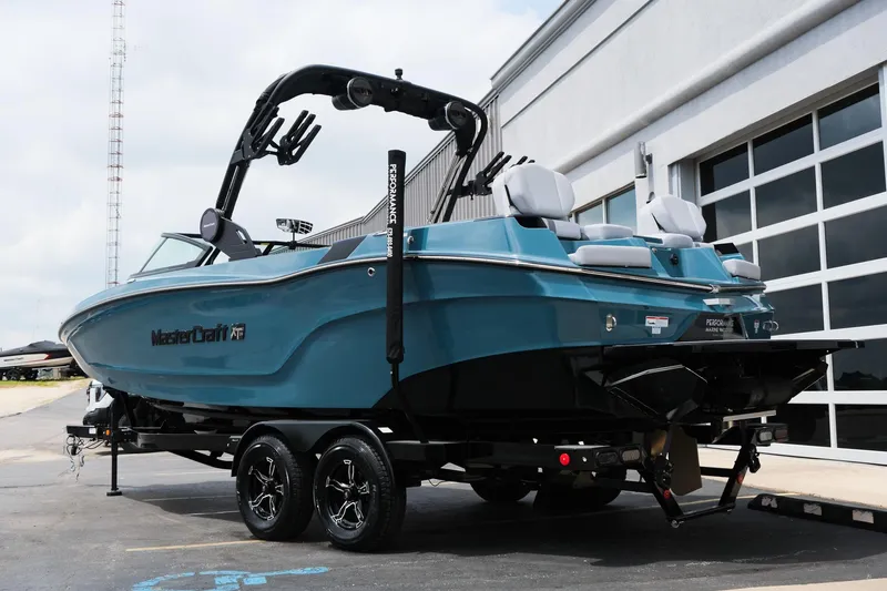 Slide: The Image of 2025 MasterCraft XT24 boat on trailer, blue exterior, parked near building. - 8