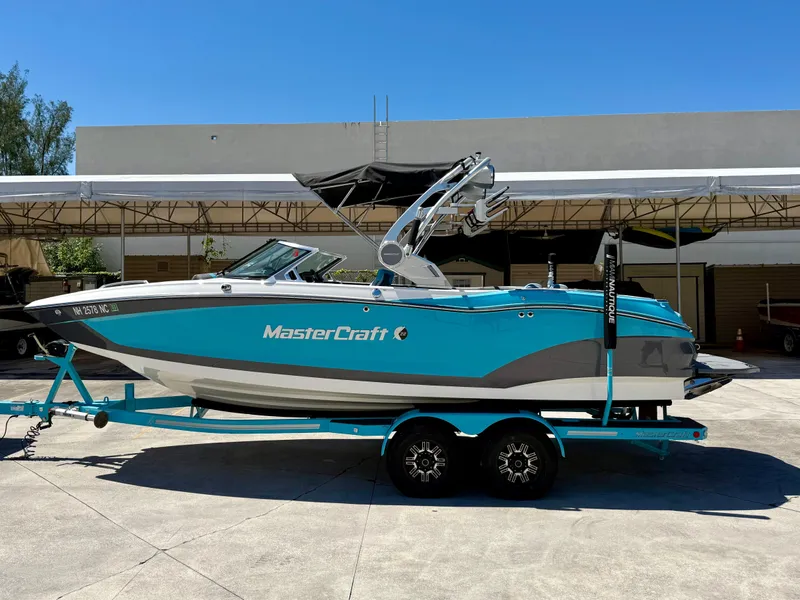 Slide: The Image of 2019 MasterCraft X22 boat on trailer, turquoise and gray, parked outdoors. - 0
