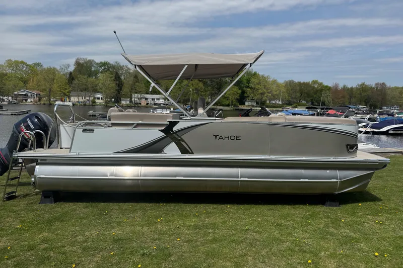 The Image of 2025 Tahoe Pontoon LTZ Quad Lounger Shift on grassy shore, with canopy and scenic background. - 0