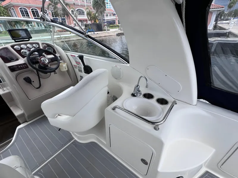 Slide: The Image of 2004 Sea Ray 260 Sundancer cockpit with steering wheel and sink, docked by waterfront. - 13