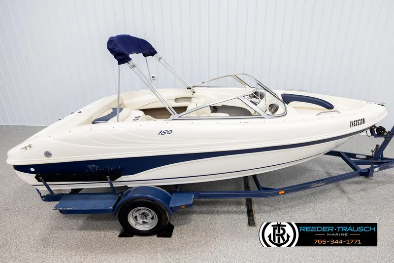 The Image of 2002 Rinker 180 boat on trailer, white and blue, displayed indoors. - 0