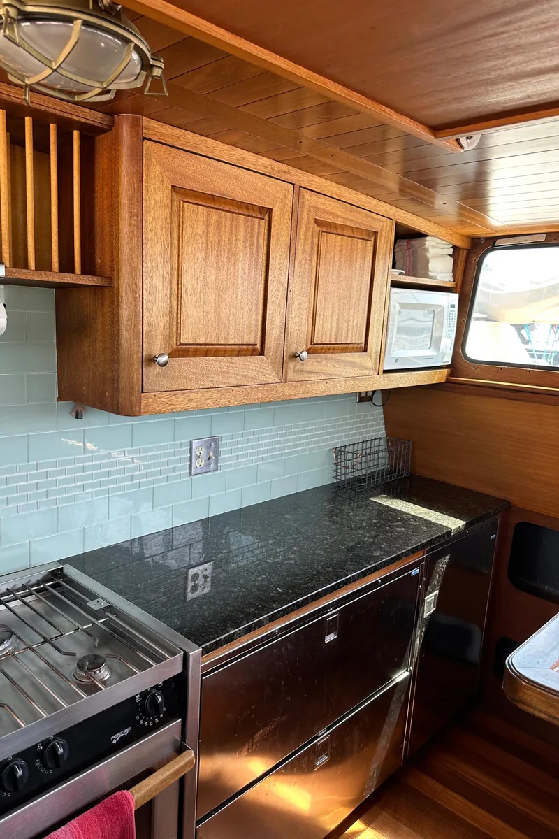 Slide: The Image of 2002 Carlson Marine Trawler kitchen with wood cabinets, granite countertop, stove, and microwave. - 30