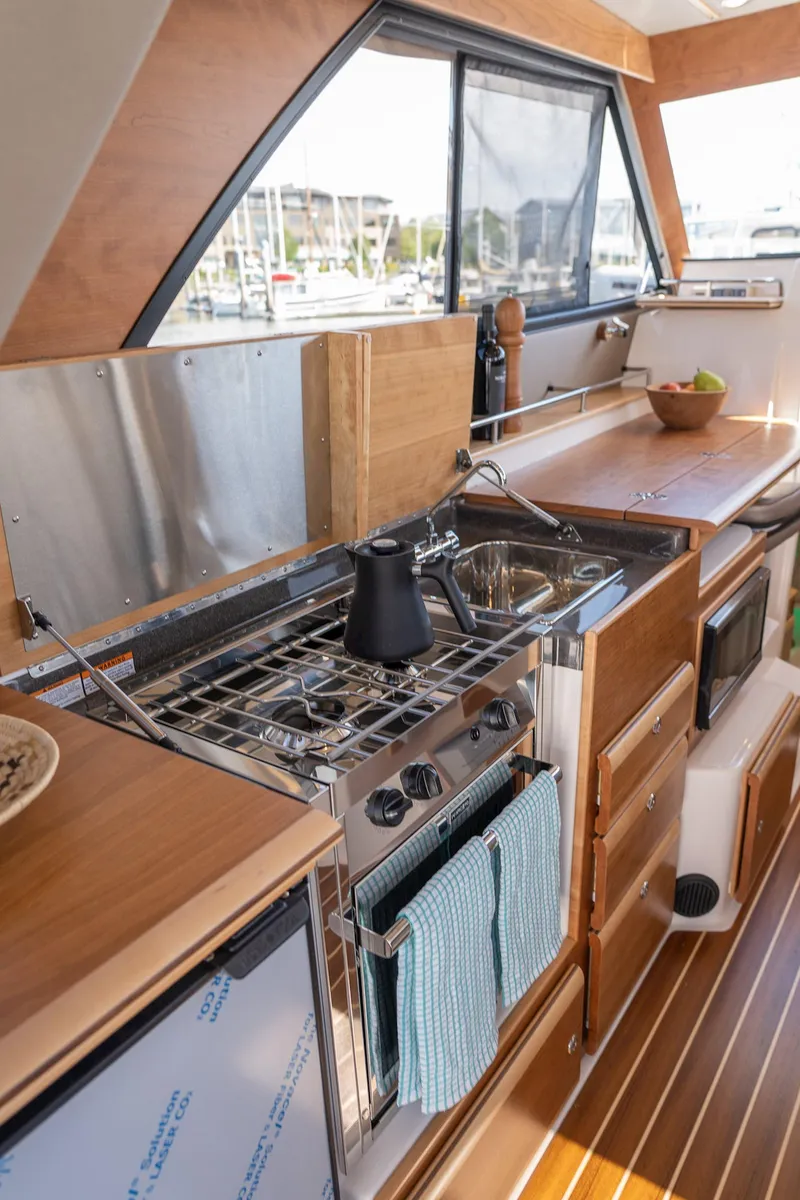 Slide: The Image of 2025 Cutwater 32 Coupe interior kitchen with stove, sink, and wooden cabinetry. - 10