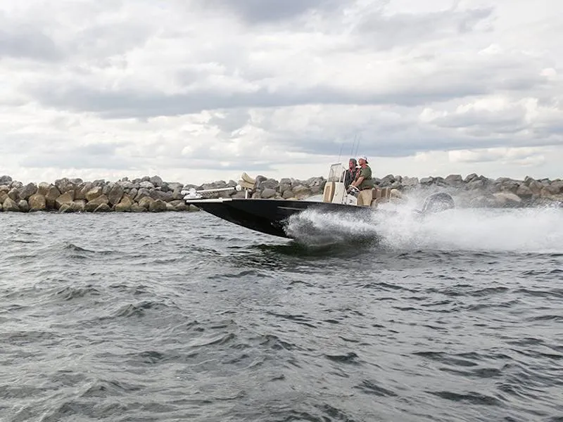 Slide: The Image of 2025 Xpress H22B boat speeding on water near rocky shoreline under cloudy sky. - 1