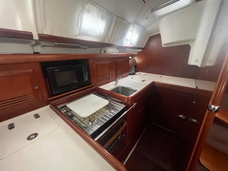 Slide: The Image of 2004 Beneteau 423 yacht kitchen with wood cabinetry, stove, sink, and microwave. - 15