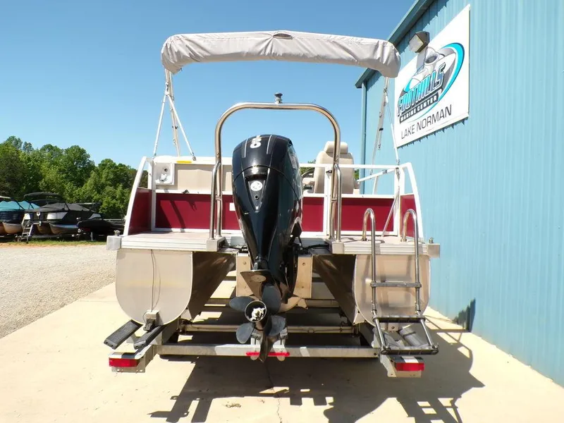Slide: The Image of 2013 JC Limited 221 Triple pontoon boat with outboard motor, parked near a blue building. - 5