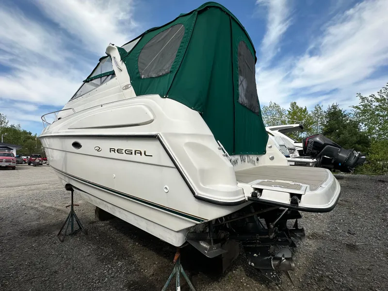 Slide: The Image of 1998 Regal 2760 Commodore boat with green canopy, parked on gravel under a blue sky. - 5