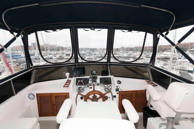 Slide: The Image of 1988 Marine Trader 48 Trawler helm with marina view, featuring classic wooden steering wheel. - 10