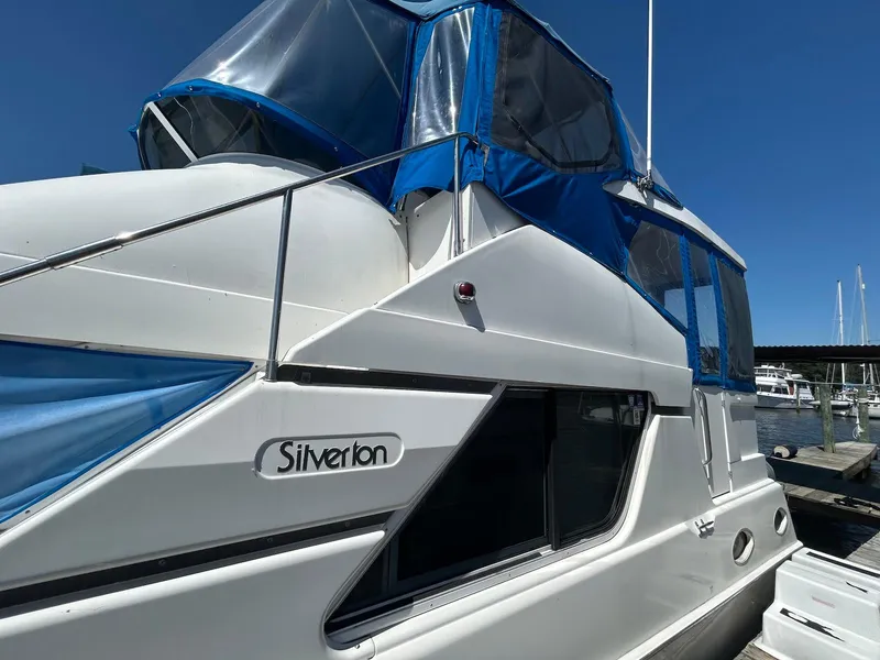 Slide: The Image of 1997 Silverton 372 Motor Yacht with blue canopy, docked under clear sky. - 6