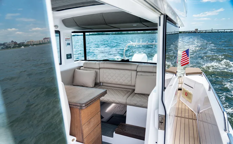 Slide: The Image of 2022 Axopar XC Aft Cabin boat interior with seating, wooden table, and American flag on water. - 15