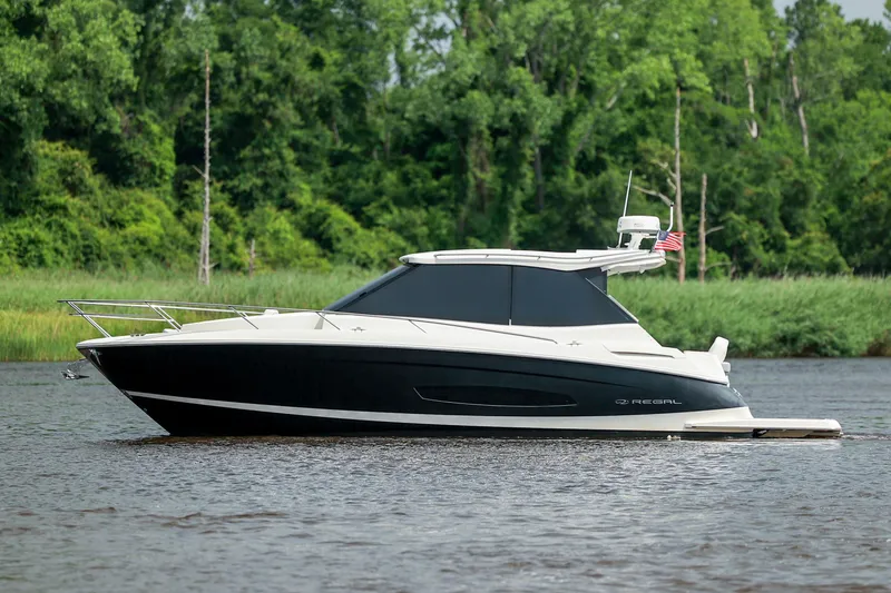 Slide: The Image of 2022 Regal 36 Grande Coupe yacht cruising on a serene river with lush green trees. - 26