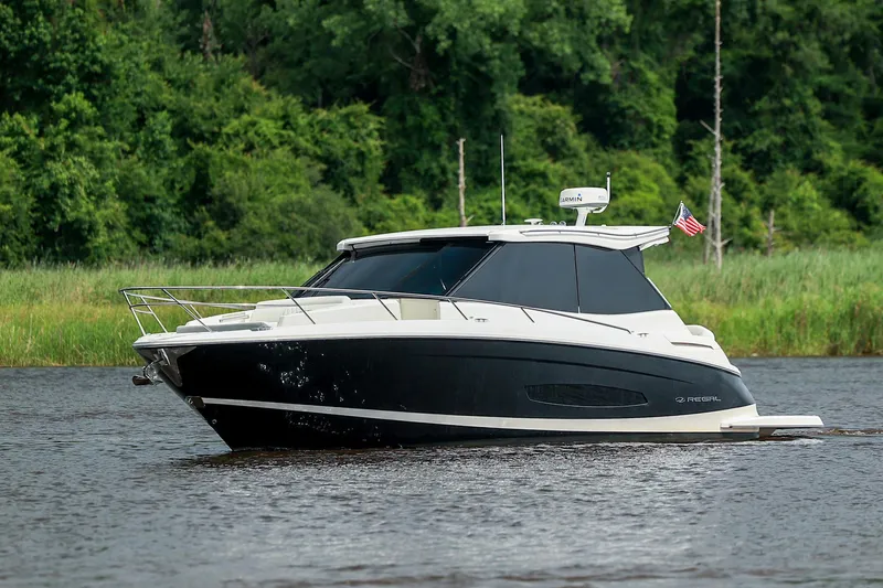 Slide: The Image of 2022 Regal 36 Grande Coupe boat cruising on a river with lush green background. - 27