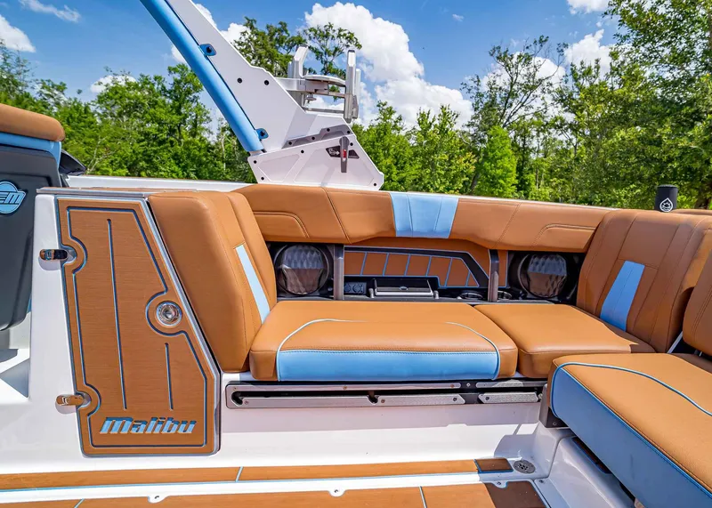 Slide: The Image of 2024 Malibu Wakesetter 24 MXZ interior with tan and blue seating, surrounded by lush greenery. - 31