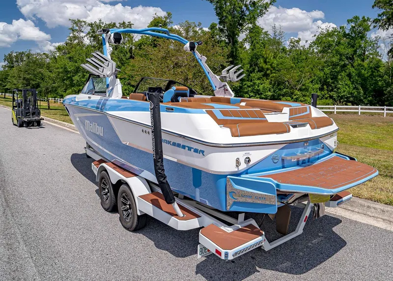 Slide: The Image of 2024 Malibu Wakesetter 24 MXZ boat on trailer, parked on a sunny road. - 4