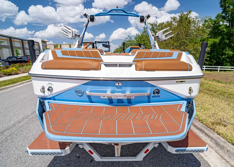 Slide: The Image of 2024 Malibu Wakesetter 24 MXZ boat, rear view, brown and blue accents, parked outdoors. - 8