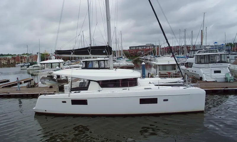 Slide: The Image of 2019 Lagoon 42 catamaran docked at marina, surrounded by other boats under cloudy skies. - 1