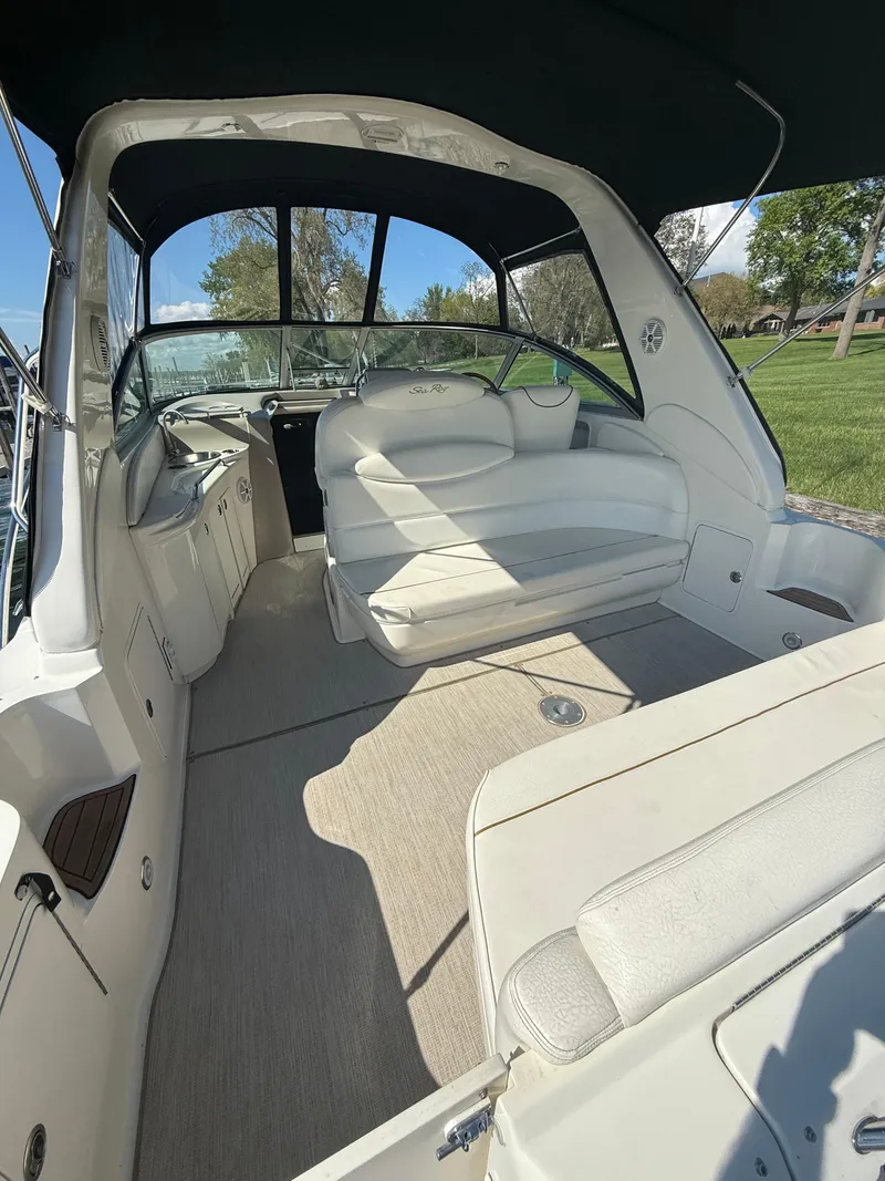 Slide: The Image of 1999 Sea Ray 340 Sundancer interior with white seating and canopy, docked near greenery. - 10