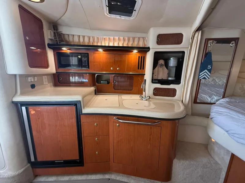 Slide: The Image of 1999 Sea Ray 340 Sundancer interior kitchen with wood cabinetry, microwave, and compact fridge. - 26