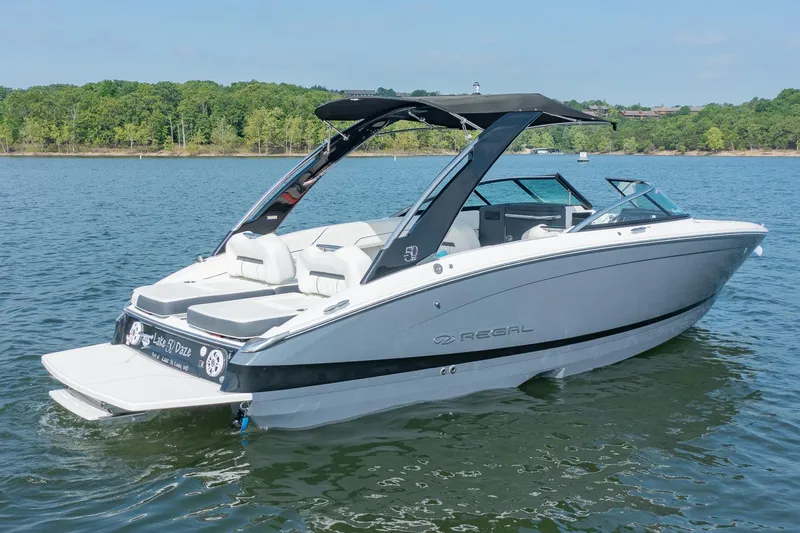 Slide: The Image of 2021 Regal LS6 boat on a serene lake with lush green shoreline. - 2