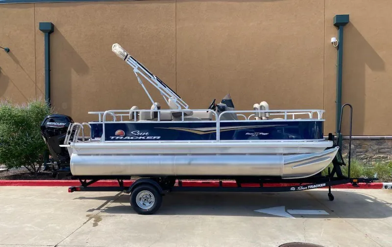 Slide: The Image of 2025 Sun Tracker Bass Buggy 18 DLX pontoon boat on trailer, parked outdoors. - 3