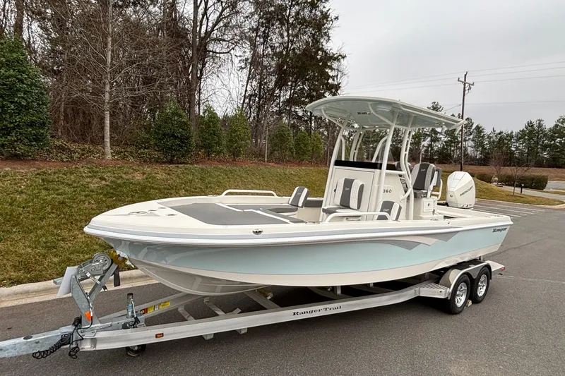 Slide: The Image of 2025 Ranger 2360 Bay boat on trailer, parked outdoors near trees. - 2