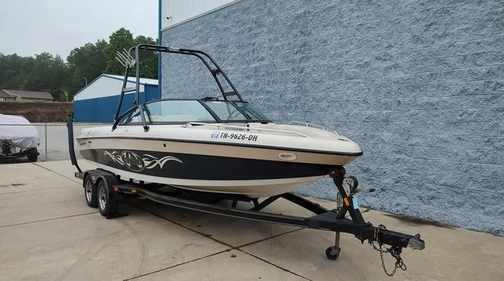 Slide: The Image of 2002 Malibu 23 LSV boat on trailer, parked beside a blue building. - 11
