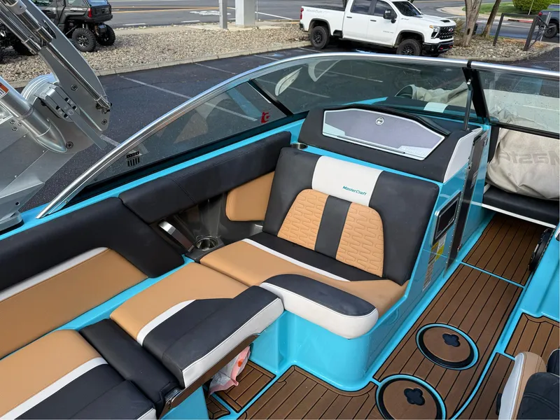Slide: The Image of 2019 MasterCraft X24 boat interior with tan and black seating, blue accents, and teak flooring. - 25