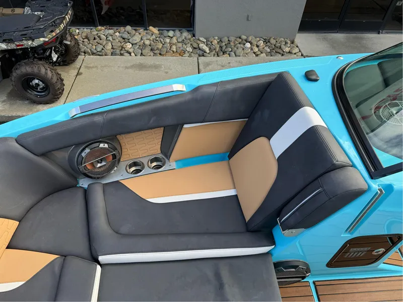 Slide: The Image of 2019 MasterCraft X24 boat interior with blue, tan, and gray seating, featuring cup holders and speaker. - 27