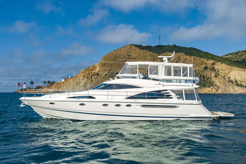 Slide: The Image of 2002 Fairline Squadron 58 yacht cruising near a rocky coastline under a clear blue sky. - 6