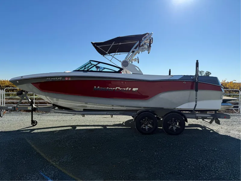 Slide: The Image of 2022 MasterCraft XT24 boat on trailer, red and white design, sunny day. - 0