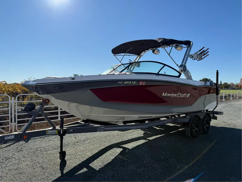 Slide: The Image of 2022 MasterCraft XT24 boat on trailer under clear blue sky. - 1